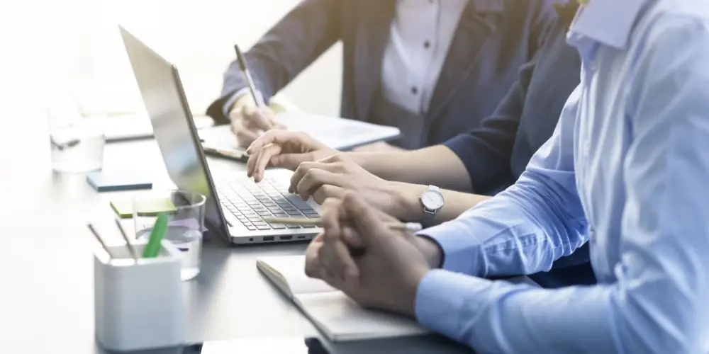 Photograph of sales reps at desks holding pens and pencils